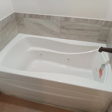 New white bathtub with modern bronze fixtures and grey tiled walls.