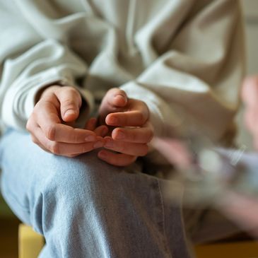 Person sitting with hands gently clasped, wearing casual clothing.