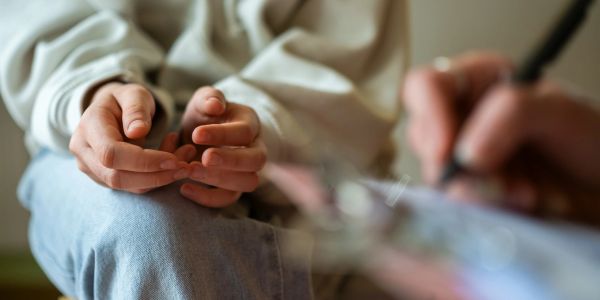 Person sitting with hands clasped, engaged in a conversation or therapy session.