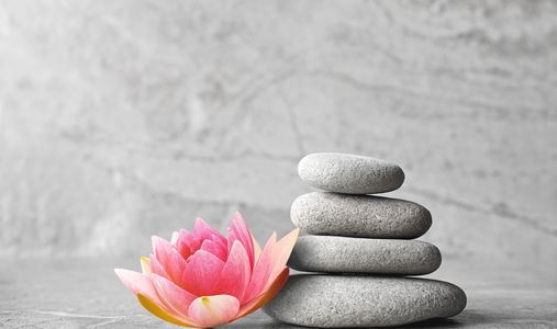 Stacked smooth stones next to a pink lotus flower symbolizing balance and tranquility.