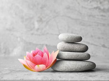Stack of smooth gray stones next to a vibrant pink lotus flower on a gray surface.