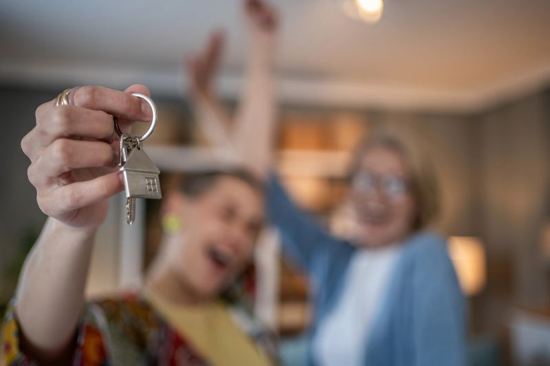 Two joyful homeowners, a mother and daughter, celebrating the milestone of buying their new home together, proudly holding their new house keys as they mark this special moment in their lives.