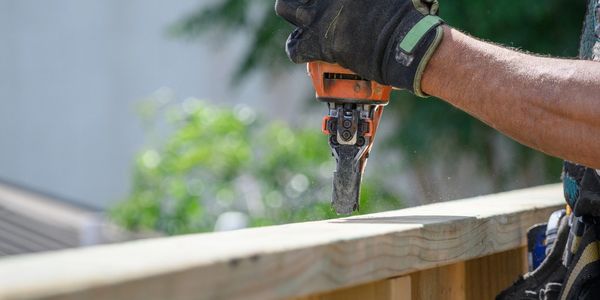 Construction worker using a nail gun on a wooden fence.