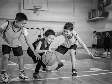 Three boys playing basketball indoors, focused on dribbling the ball.
