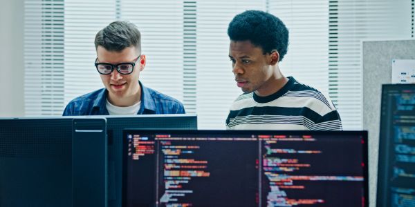 Two programmers working together at multiple monitors.