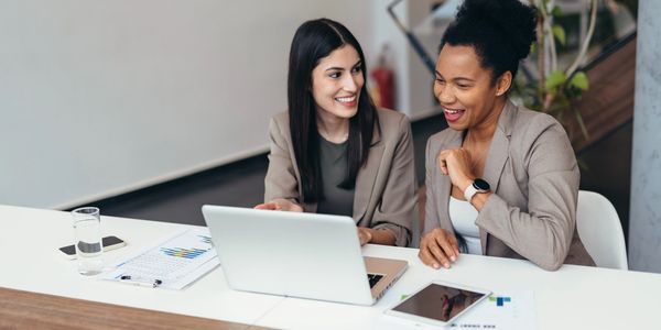 Two professional women smiling and discussing work at a laptop.