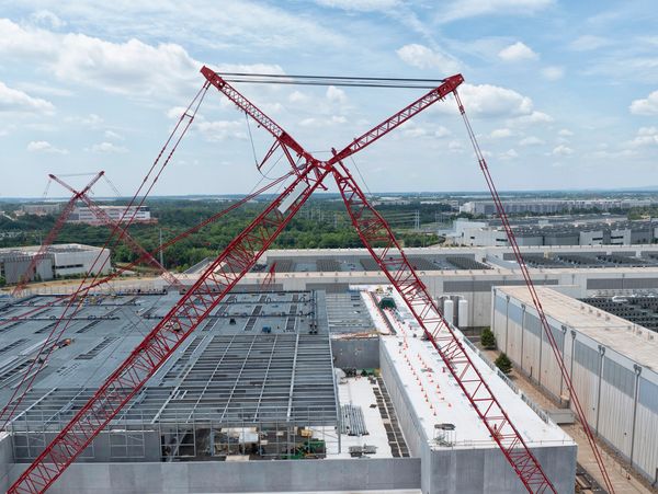 Two large red cranes at a construction site with industrial buildings in the background.