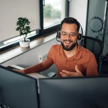 Man in headset working with dual monitors in a bright office.