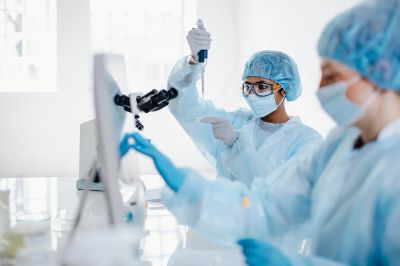 Scientists in protective gear conducting lab research using pipettes and microscopes.