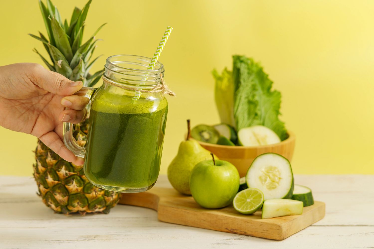 Hand holding a green smoothie jar with fresh fruits and vegetables.