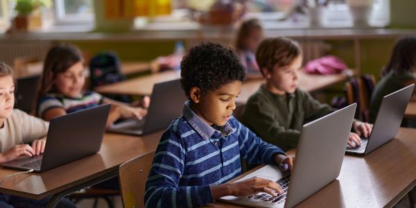 Children focused on laptops in a classroom setting.