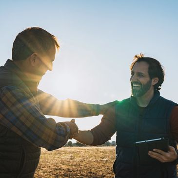 Two men shaking hands outdoors with the sun shining behind them.