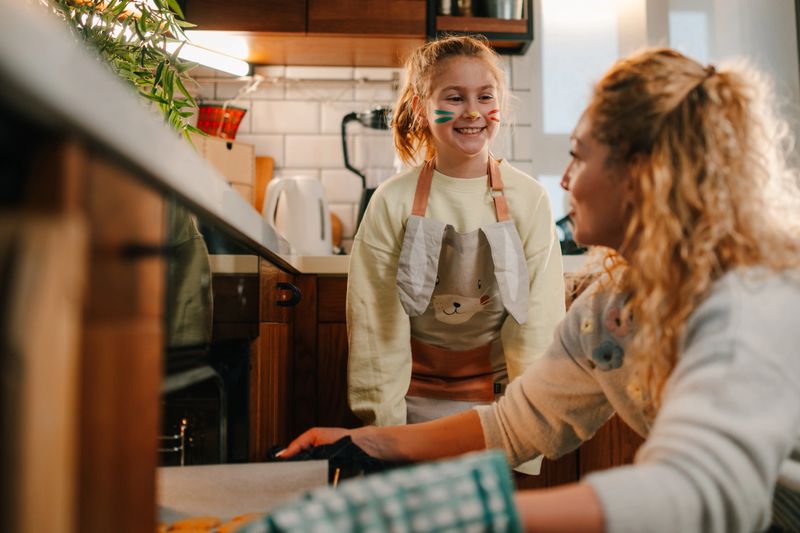 Mother and daughter baking cookies together in a modern kitchen, joyfully taking the tray out of the oven and sharing smiles, creating cherished memories in a warm, loving environment