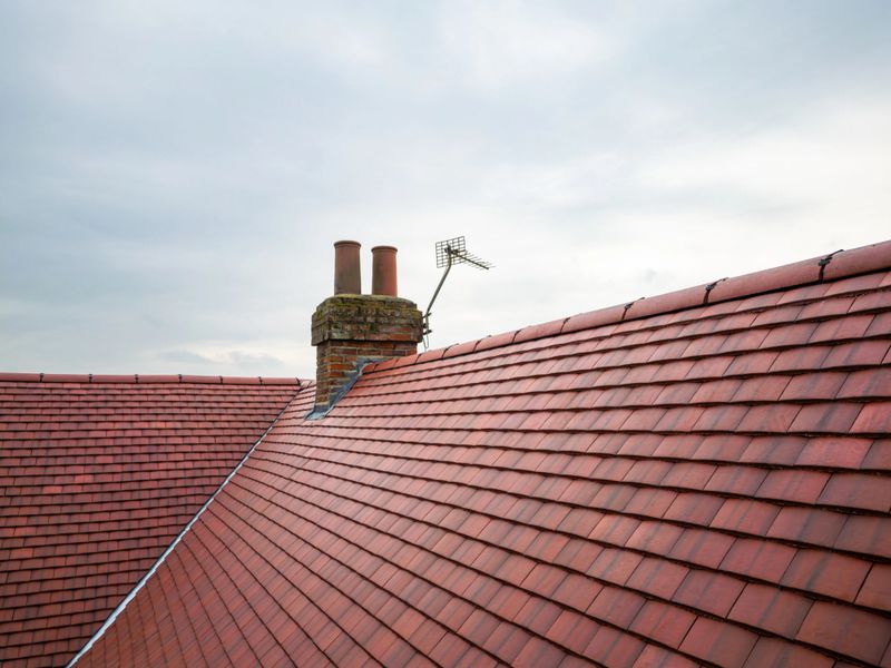 Inspection drone view of a newly installed ceramic roof on an old English farmhouse. The old, brick built chimney stack is visible.