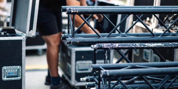 Stacked metal trusses and equipment cases with person in background.