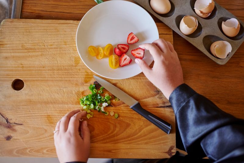 Person, hands or strawberry with chopping board above for healthy diet, meal preparation or vegetarian snack at home. Top view, fruit and vegan with organic food, eggs or chives for vitamin nutrition