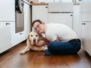 Man cuddling with his dog on the kitchen floor.