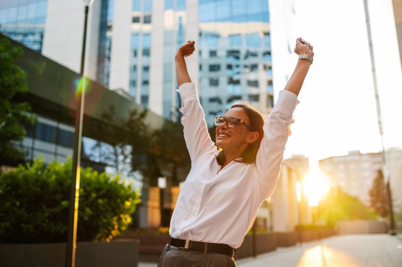 Successful businesswoman celebrates a career achievement in a vibrant city setting at sunset, exuding confidence and motivation as a true leader