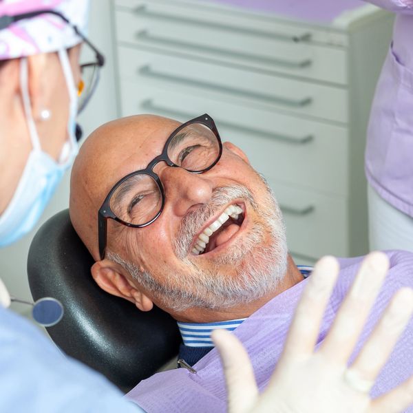 Smiling elderly man at the dentist's office receiving care.