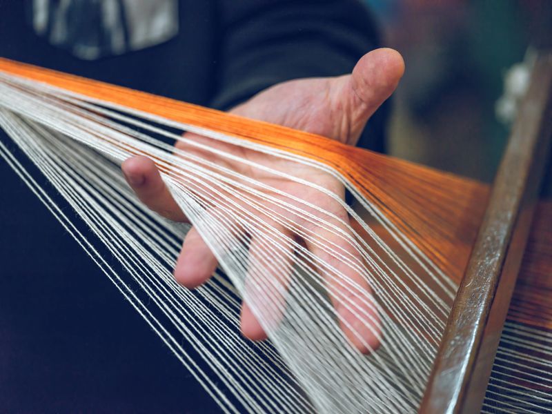 Close-up of hands weaving threads on a loom in a textile workshop