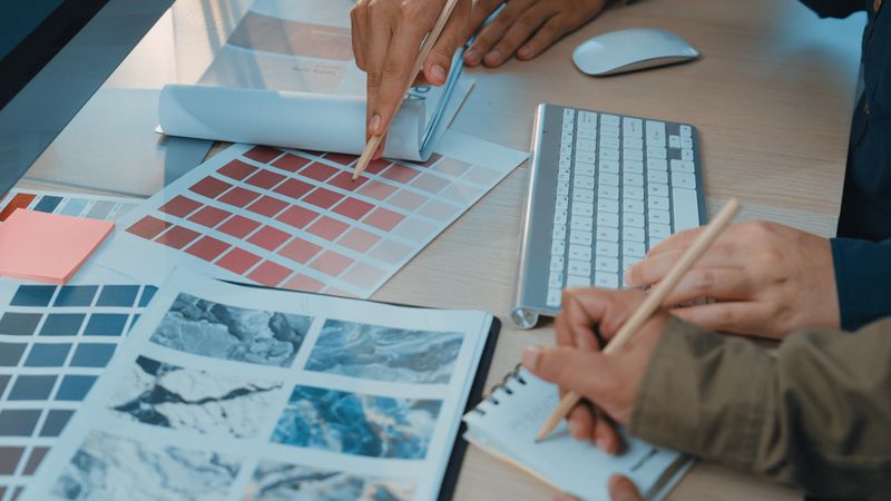 Two creative professionals engage in a collaborative process, selecting color palettes and reviewing design materials in a modern workspace filled with digital tools. SACTR