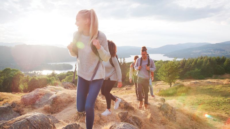 Multi-Cultural Group Of Young Friends Walking Along Hill Ridge Hiking In UK Lake District
