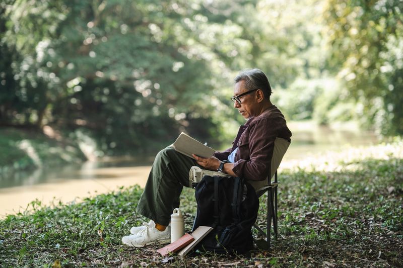 Senior author immersing himself in a book, seeking inspiration amidst the peaceful surroundings of his wellness trip, reflecting deeply, jotting down thoughts and ideas that come to mind