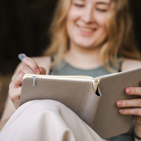 A smiling woman writing in a journal outdoors.