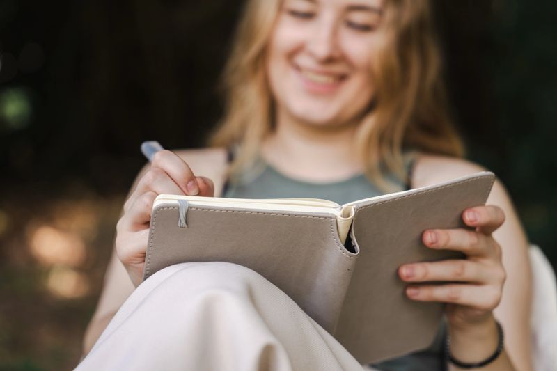 A young woman sitting on a camping chair, journaling her thoughts and creative ideas in a notebook, drawing inspiration from the natural scenery surrounding her