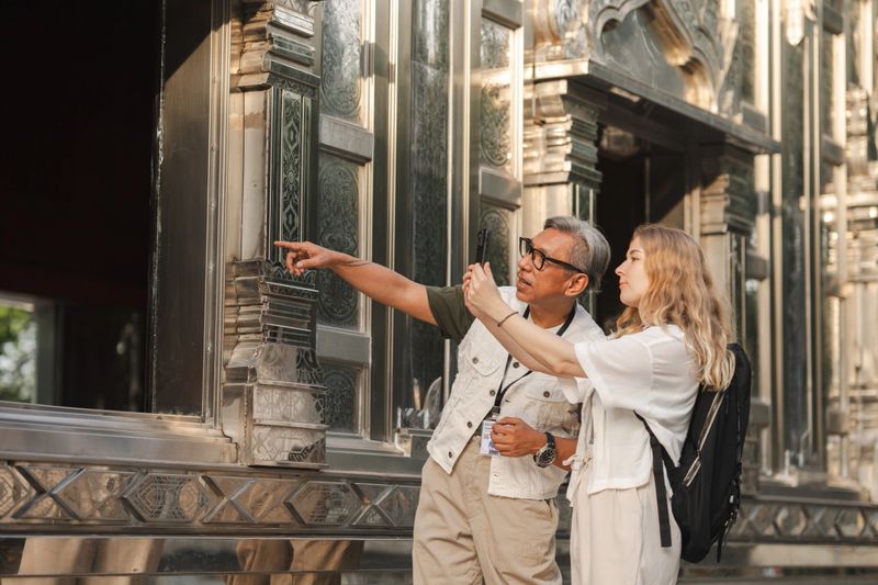 A foreign tourist listening attentively while learning about the history of the temple from a local senior tour guide