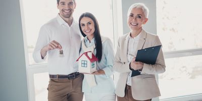 Happy couple holding house keys and model with real estate agent.