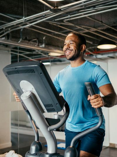 A smiling man exercises on an elliptical machine in a gym.