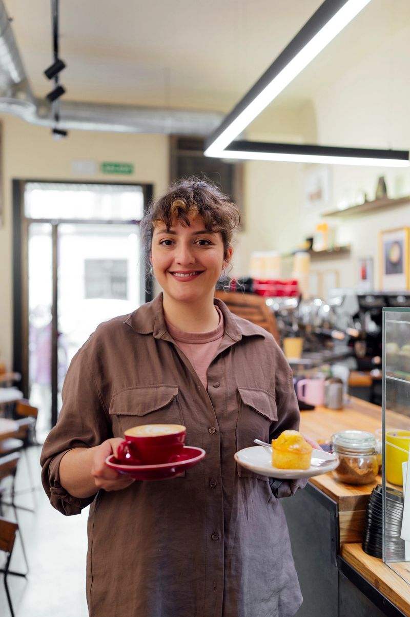 Smiling waitress holding cappuccino and muffin, working in cafeteria
