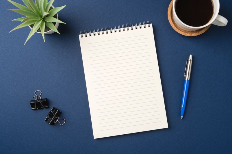 Top view of a workspace with a blank notebook, pen, coffee, and plant