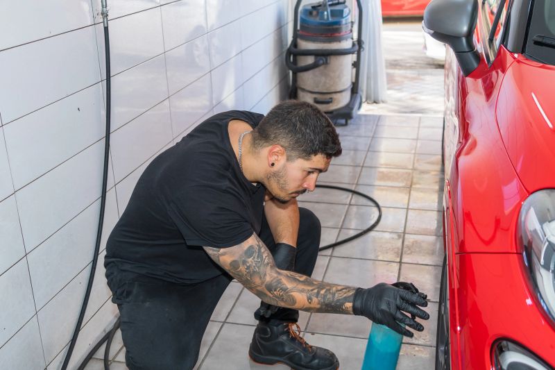 Professional car detailer applying cleaning solution to a red car's exterior in a car wash facility. Focused on precision and quality.