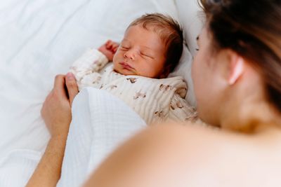 A newborn baby sleeps peacefully next to a parent in a cozy bed.