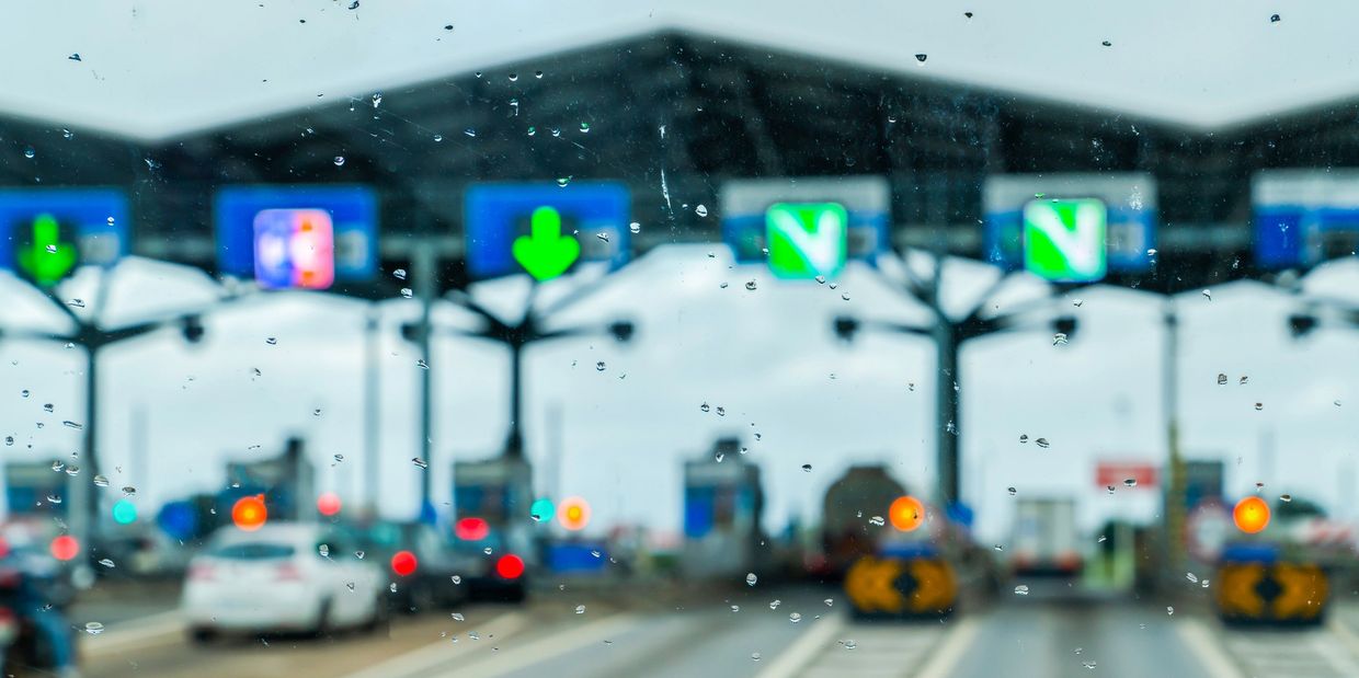 Raindrops on windshield at a toll booth with blurred traffic.