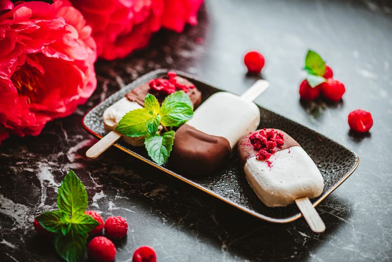 Delicious homemade vanilla ice-cream popsicles with raspberries and chocolate and peonies in the background