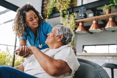 Nurse smiling warmly at elderly woman in cozy home setting.