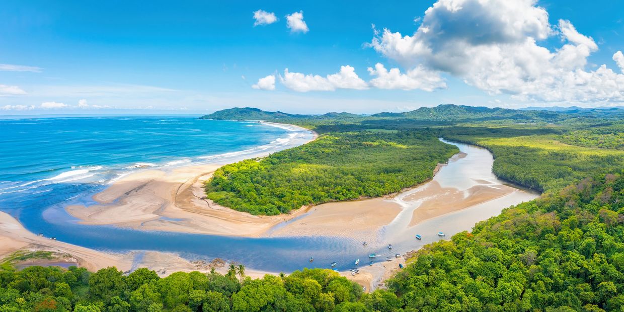 A river flowing into the ocean surrounded by lush greenery under a blue sky.
