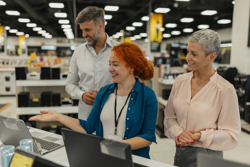Two customers explore electronics alongside a sales assistant, fostering a positive shopping experience through informative discussions about products and features.