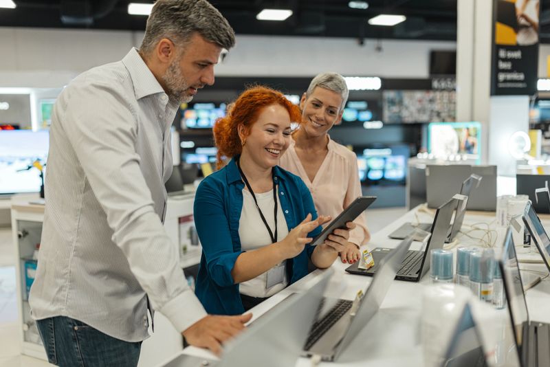 Engaged customers are seen discussing electronics with a sales representative amidst a vibrant retail environment filled with the latest tech products and displays.