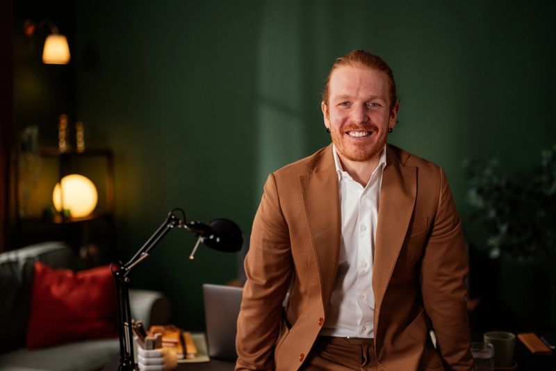 Portrait of a smiling businessman sitting on his desk in his home office, looking at the camera