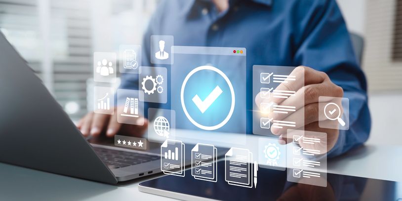 Person interacting with digital checklists and data icons by a laptop and tablet.