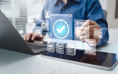 Person using digital checklist and productivity icons on tablet and laptop.