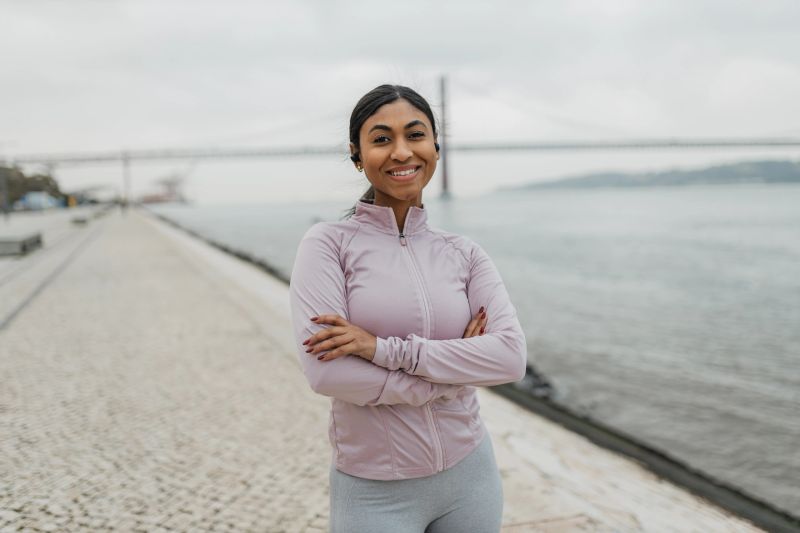 A charming woman dressed casually stands confidently with arms crossed, exuding warmth and friendliness that captures the essence of joy and comfort in her surroundings.