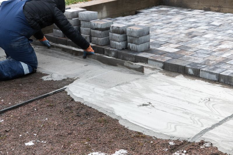 Worker installs paving bricks for an outdoor pathway, ensuring a stable and appealing surface. Practical application of construction techniques visible with neatly arranged paving block stacks