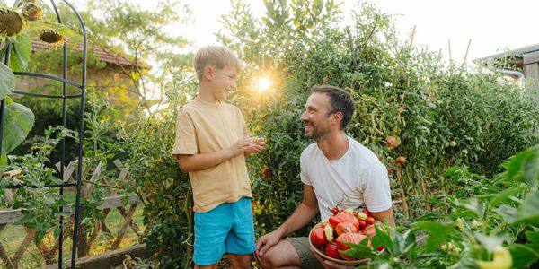 A father and son smiling in a garden with fresh vegetables.