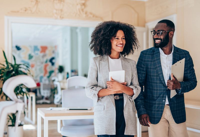 Shot of two coworkers having a discussion in modern office. Businessman and businesswoman in meeting discussing business strategy while walking in an office. Confident business people working together in the office. Creative business persons discussing new project and sharing ideas in the workplace.