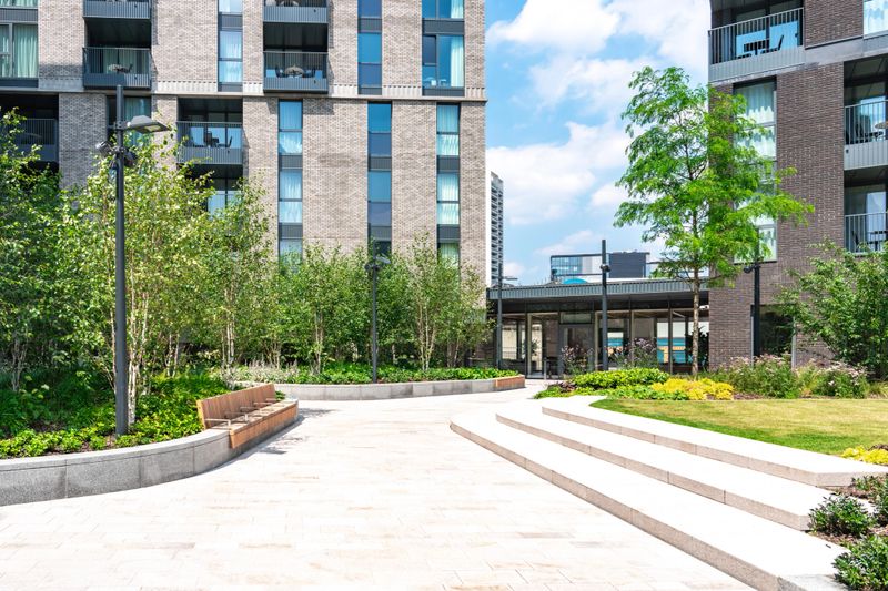 Empty courtyard of a modern residential complex with benches, trees, and paved walkways